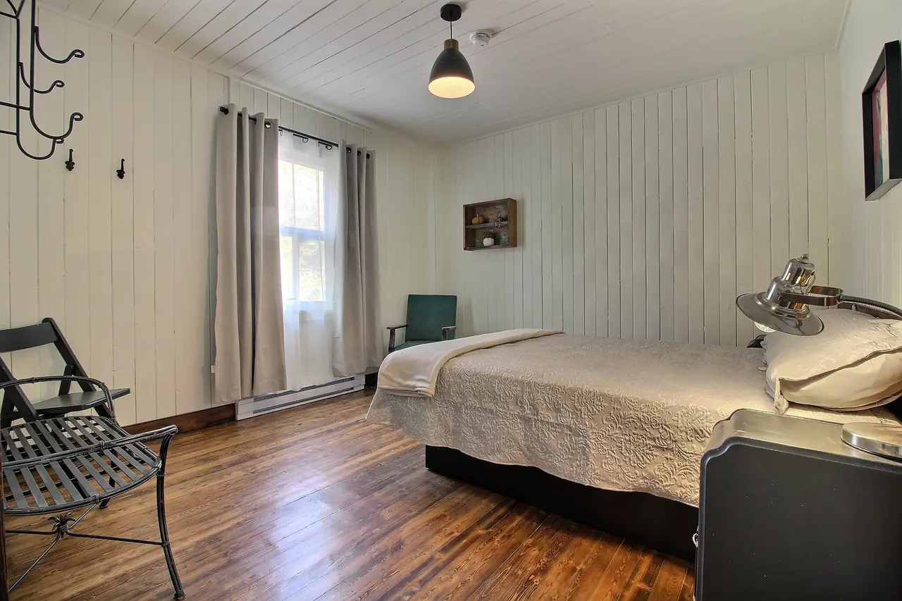 La chambre du commis : lit queen, murs de planches claires et plancher de bois d'origine.