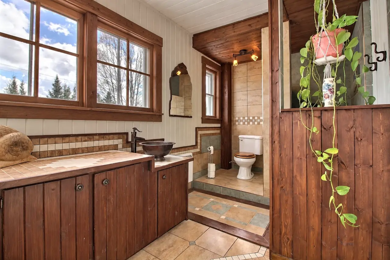 La salle de bain complète : vasque de cuivre, comptoir de tuiles, grandes fenêtres et la toilette au fond.